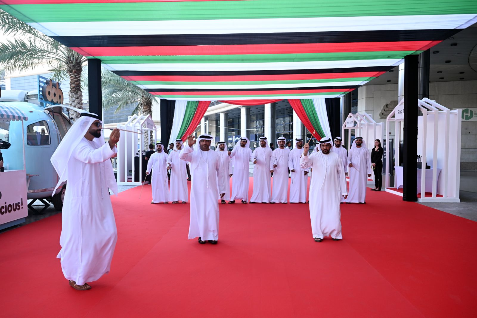 UAE National Day event organized by M&M Group, featuring a traditional Emirati dance performance on a red carpet under a canopy decorated with the UAE flag colors. The event showcases Emirati heritage with participants in traditional attire, highlighting the cultural richness and national pride of the UAE in a festive and well-coordinated celebration.